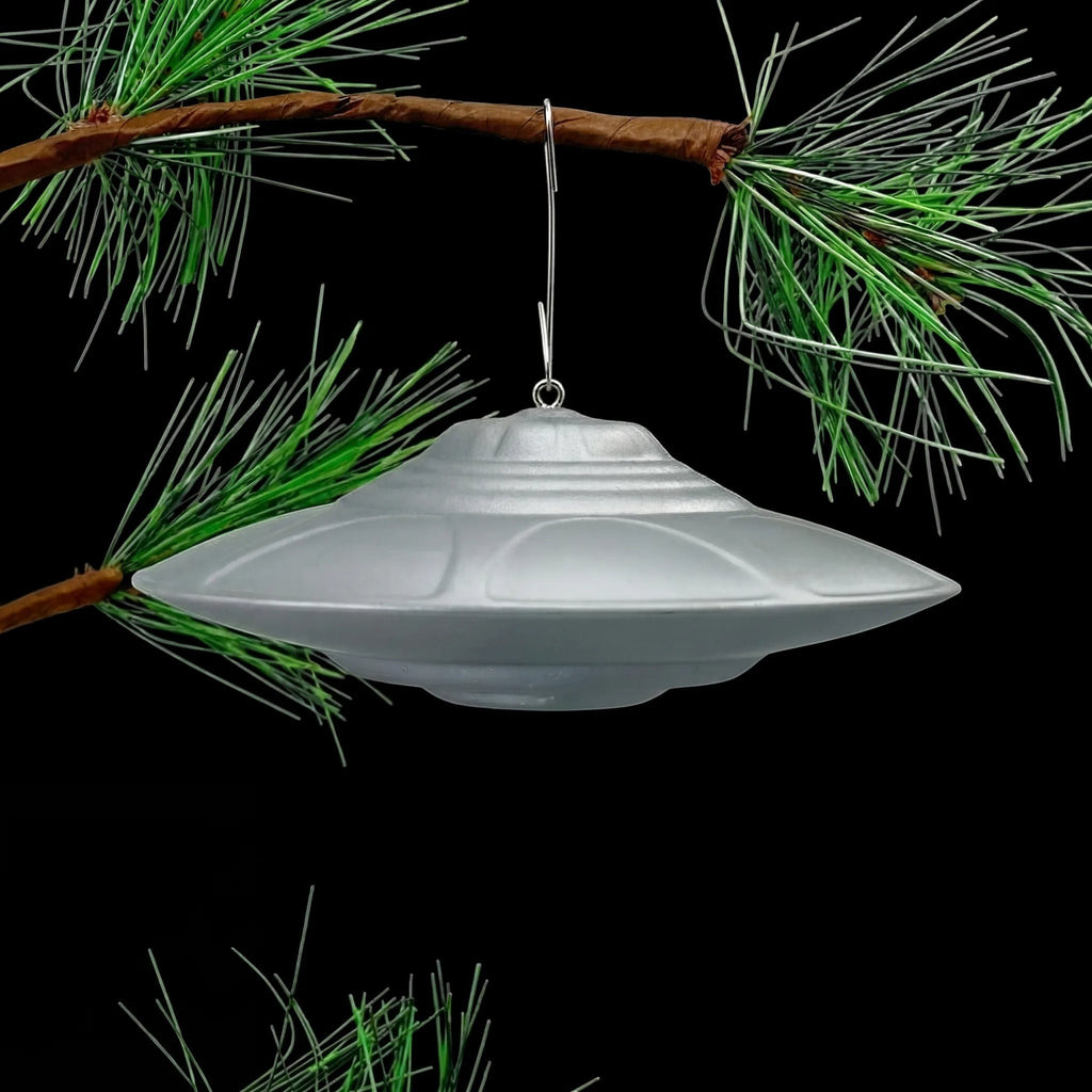Classic Flying Saucer UFO ornament hanging from pine tree branch, lifestyle display shot