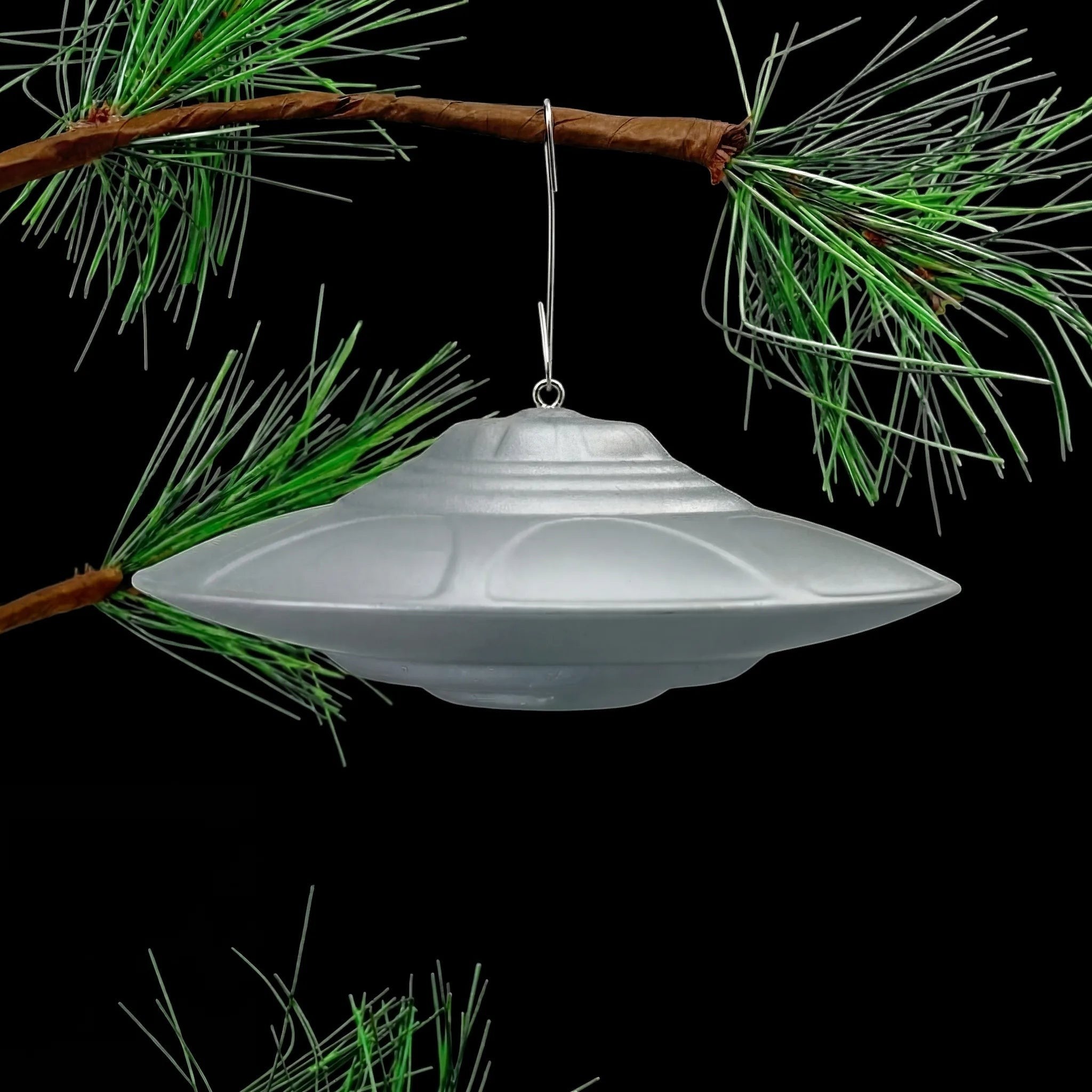 Classic Flying Saucer UFO ornament hanging from pine tree branch, lifestyle display shot