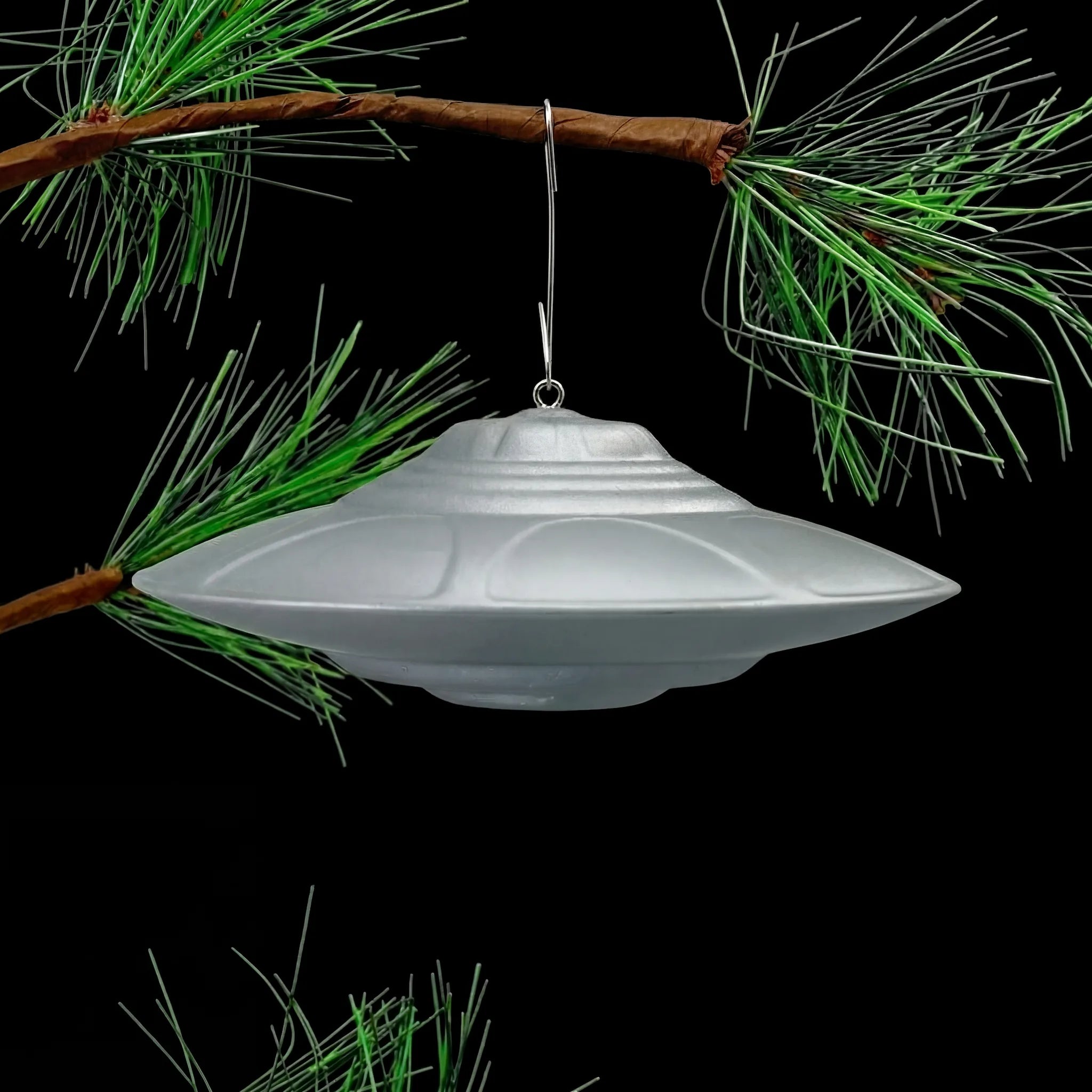 Classic Flying Saucer UFO ornament hanging from pine tree branch, lifestyle display shot